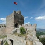 Taş kale kulesi, surlar ve tepede dalgalanan Türk bayrağı