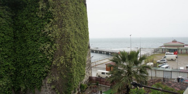 Yağmurlu havada sarmaşıkla kaplı taş kule ve arkasında deniz