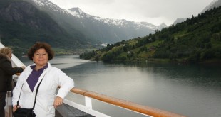 Gemi güvertesinde karlı dağlarla çevrili fiyortu izleyen kadın