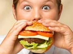Elleriyle büyük hamburger yiyen şaşkın bakışlı çocuk