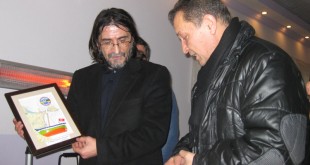 Salonda plaket tutan erkek ve yanında ceketli başka bir erkek