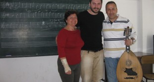 Müzik sınıfında tahta önünde ud tutan erkek ve yanındaki iki kişi
