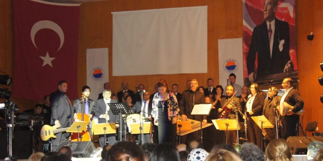 Türk bayrağı ve büyük portre altında sahnede müzik topluluğu