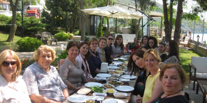 Çam ağaçları altında uzun yemek masasında oturan kadınlar