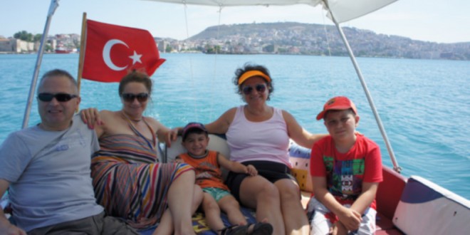 Bayraklı teknede oturan yetişkinler ve çocuklar, arkada kıyı şehri