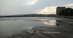Alçalmış deniz suyu, kıyıdaki tarihi kale burcu ve bulutlu gökyüzü