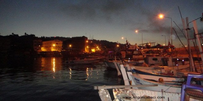 Gece balıkçı limanında tekneler, ışıklar ve suya yansıyan aydınlık