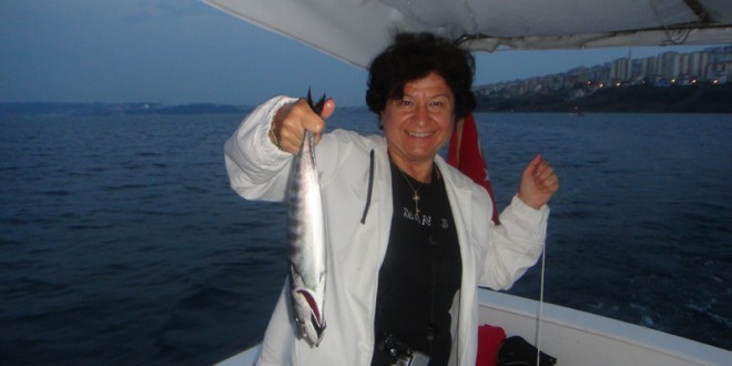 Teknede yakaladığı balığı tutup gösteren beyaz ceketli kadın