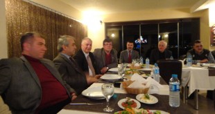 Uzun yemek masasında oturan erkekler, önlerinde salata ve tabaklar