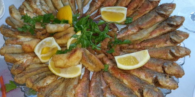 Büyük tabakta limon dilimleri ve maydanozla servis edilen kızarmış balıklar