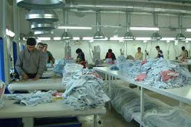 Tekstil atölyesinde uzun masalarda çalışan işçilerin görüntüsü