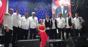 Konser sahnesinde beyaz gömlekli müzisyenler ve kırmızı elbiseli solist