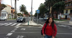 Tenerife'de palmiyeli caddede kırmızı montlu gülümseyen kadın