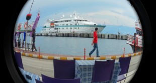 Balık gözü lensle çekilmiş iskele, mor sandalyeler ve limandaki beyaz yolcu gemisi