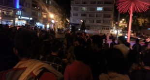 Gece şehirde caddede toplanmış kalabalık ve arkadaki ışıklı binalar