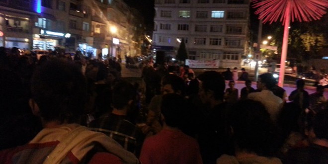 Gece şehirde caddede toplanmış kalabalık ve arkadaki ışıklı binalar