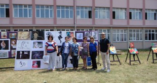 Okul bahçesinde açık hava tablo sergisinin önünde poz veren grup