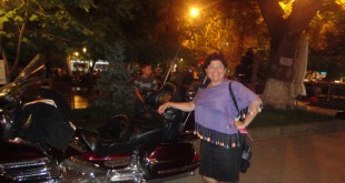Gece park alanında büyük bir motosikletin yanında poz veren kadın