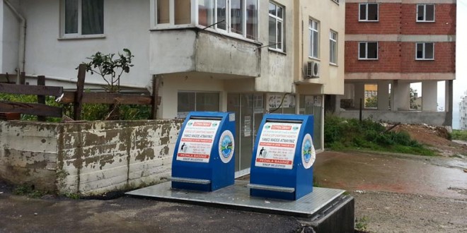 Apartman önündeki iki mavi atık yağ toplama kumbarası ve ıslak zemin