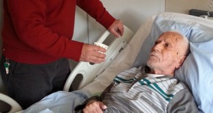 Hastane odasında yatakta yatan bir hasta ve yanında duran bir erkek