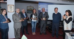 Salonda ayakta plaket tutan konuklar ve mikrofonla konuşan kadın