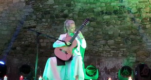 Yeşil ışıklı sahnede ayakta klasik gitar çalan kadın