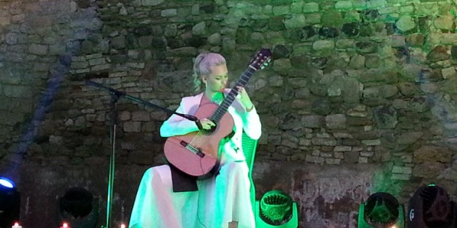 Yeşil ışıklı sahnede ayakta klasik gitar çalan kadın