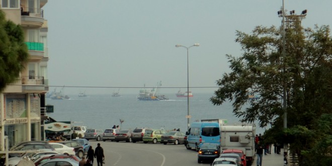 Sokakta park halindeki arabalar ve arkada deniz manzarası