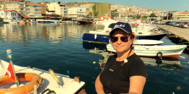 Teknede duran şapkalı kadın ve arkasında liman manzarası