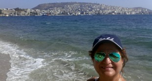 Boş bir sahilde şapkasıyla selfie çeken bir kadın.