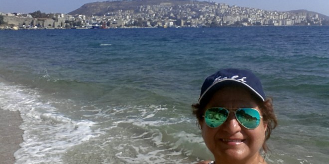 Boş bir sahilde şapkasıyla selfie çeken bir kadın.