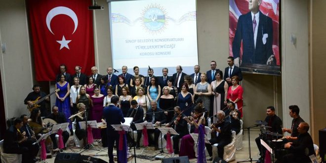 Sahnede Türk bayrağı önünde koro ve orkestra konser veriyor