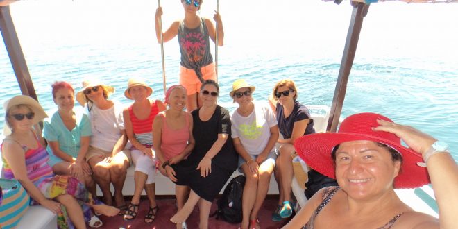 Teknede ayakta duran kırmızı şapkalı kadın ve oturan grup