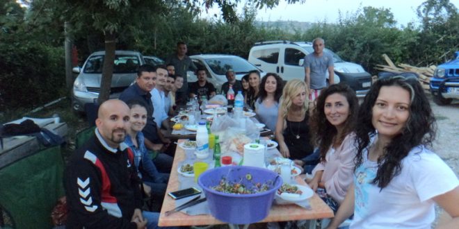 Ağaçlar altında uzun masada toplu halde yemek yiyen kalabalık