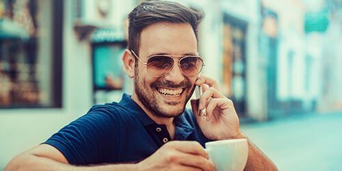 Güneş gözlüklü bir erkeğin kafede telefonla konuşurken çekilmiş görüntüsü.