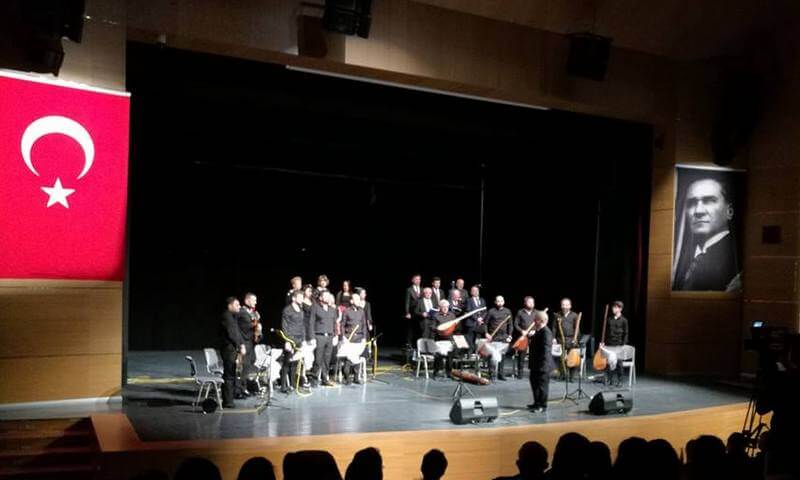 Türk bayrağı ve Atatürk portresi önünde sahnede performans sergileyen koro.