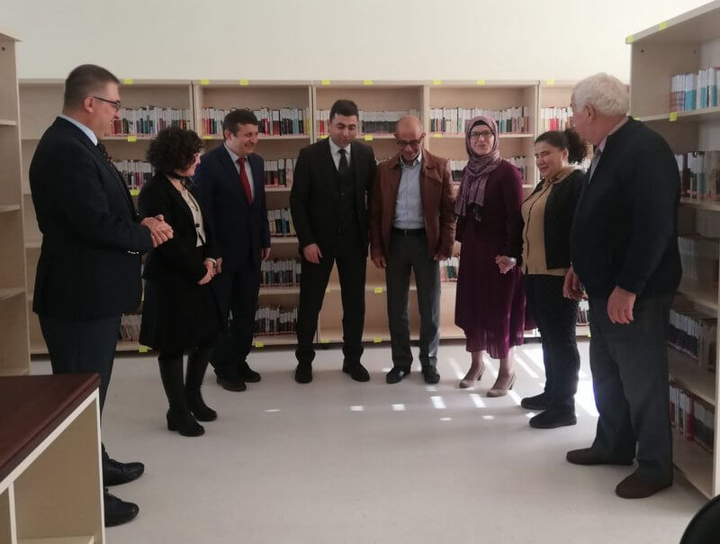 Kütüphanede raflar önünde duran bir grup ziyaretçi.