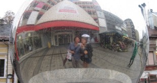 Aynalı büyük bir kürenin üzerinde yansıyan alışveriş caddesi ve iki kişi