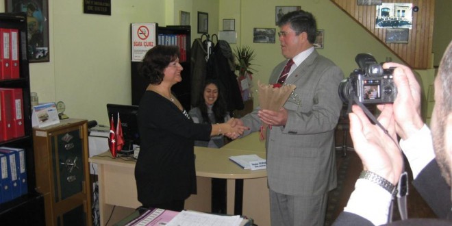Ofiste kadın ile takım elbiseli erkek çiçek eşliğinde tokalaşıyor
