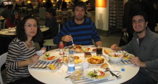Kalabalık bir restoranda yemek dolu yuvarlak masada oturan üç kişi